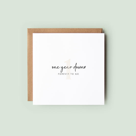Minimalist first anniversary card reading “one year down” and “FOREVER TO GO” with a subtle number 1, shown as a square white 148x148mm (6x6) card with Kraft envelope behind.