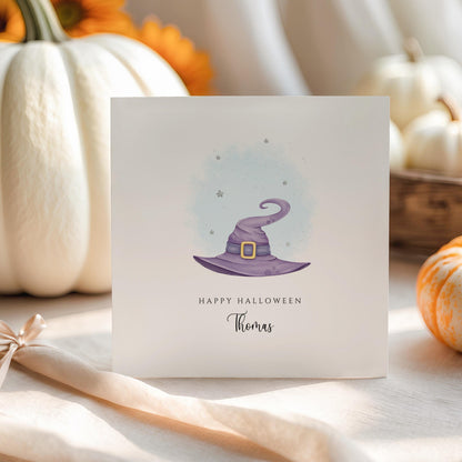 Personalised Halloween greeting card featuring a purple watercolour witch's hat with a custom name underneath and the words "Happy Halloween" on a white card.
