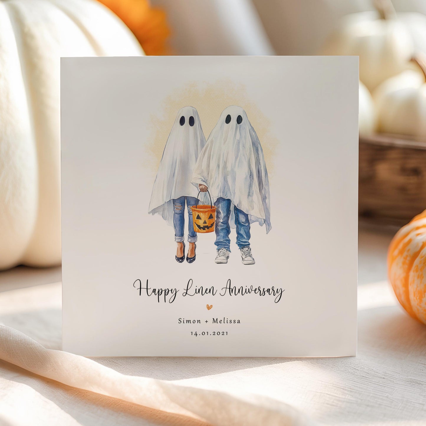 Personalised linen anniversary card featuring a ghost couple in Halloween costumes holding a pumpkin bucket, with custom names and wedding date.