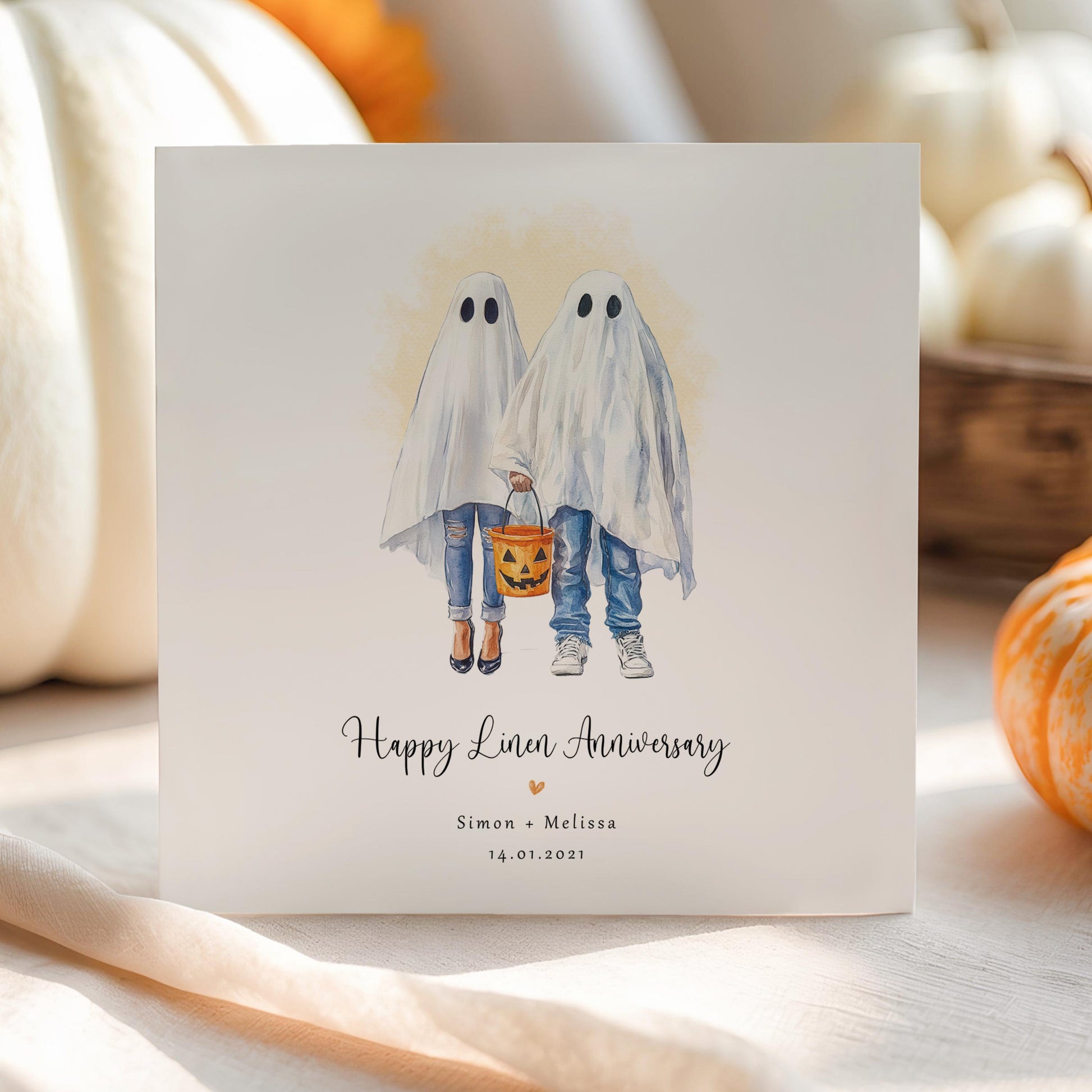 Personalised linen anniversary card featuring a ghost couple in Halloween costumes holding a pumpkin bucket, with custom names and wedding date.