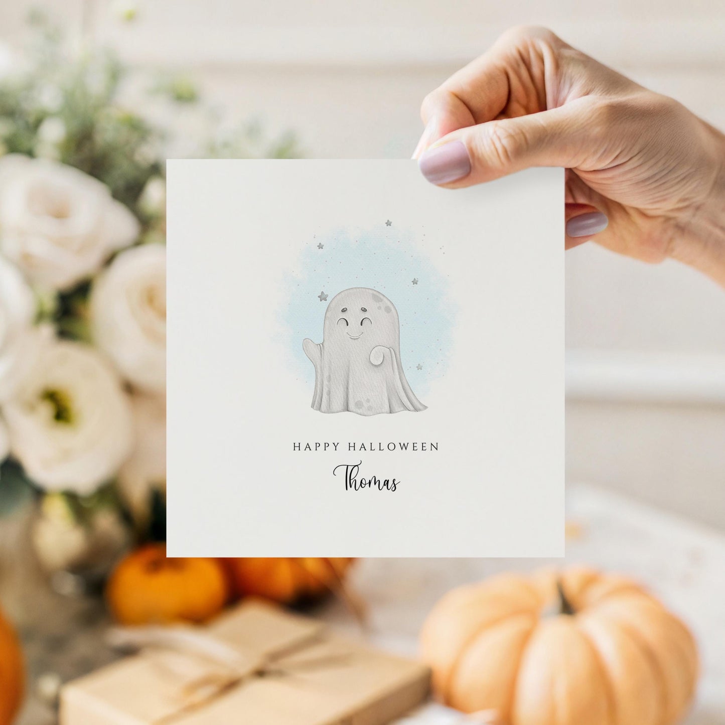 Cute Halloween card with a smiling cartoon ghost and soft blue watercolour stars, featuring the message “Happy Halloween” with a personalised name underneath