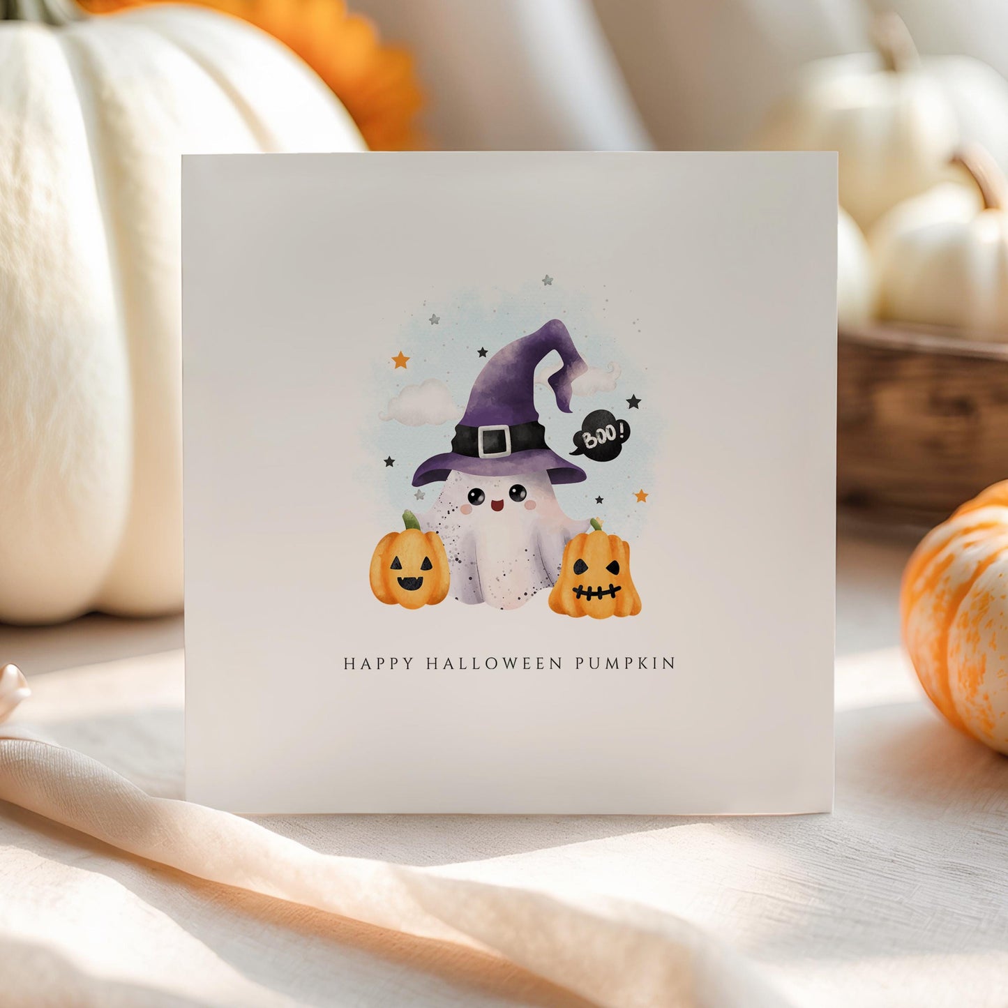 Cute Halloween card with ghost in a purple witch hat and two pumpkins, set against a soft pastel background.