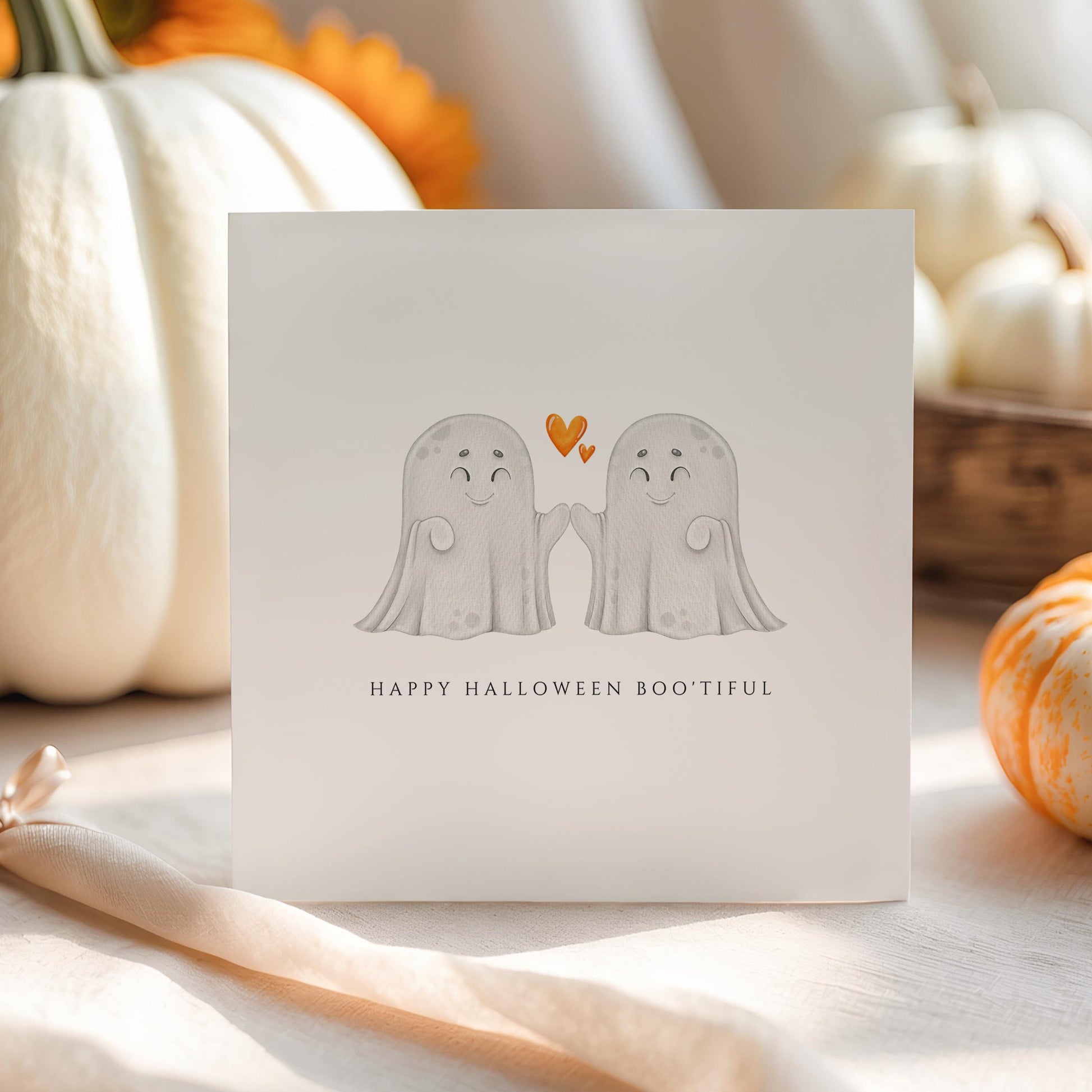 Halloween card with two cute ghost characters high-fiving and a heart above them, captioned “Happy Halloween Boo’tiful”.