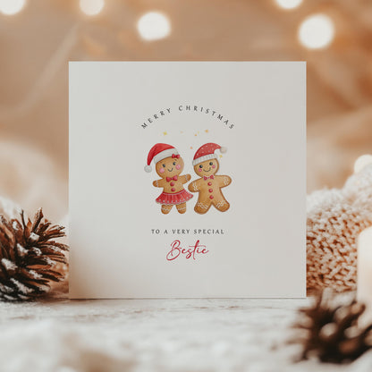 Cute Christmas card with male and female gingerbread characters in Santa hats, captioned “To a very special Bestie” – festive scene with soft lights.