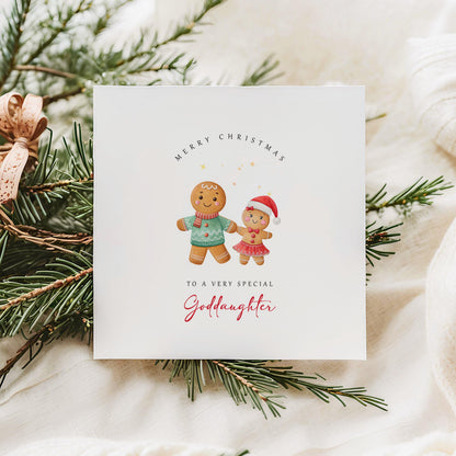Christmas card from godfather to goddaughter with two gingerbread girls in Santa hats, set against a festive, cosy holiday background.