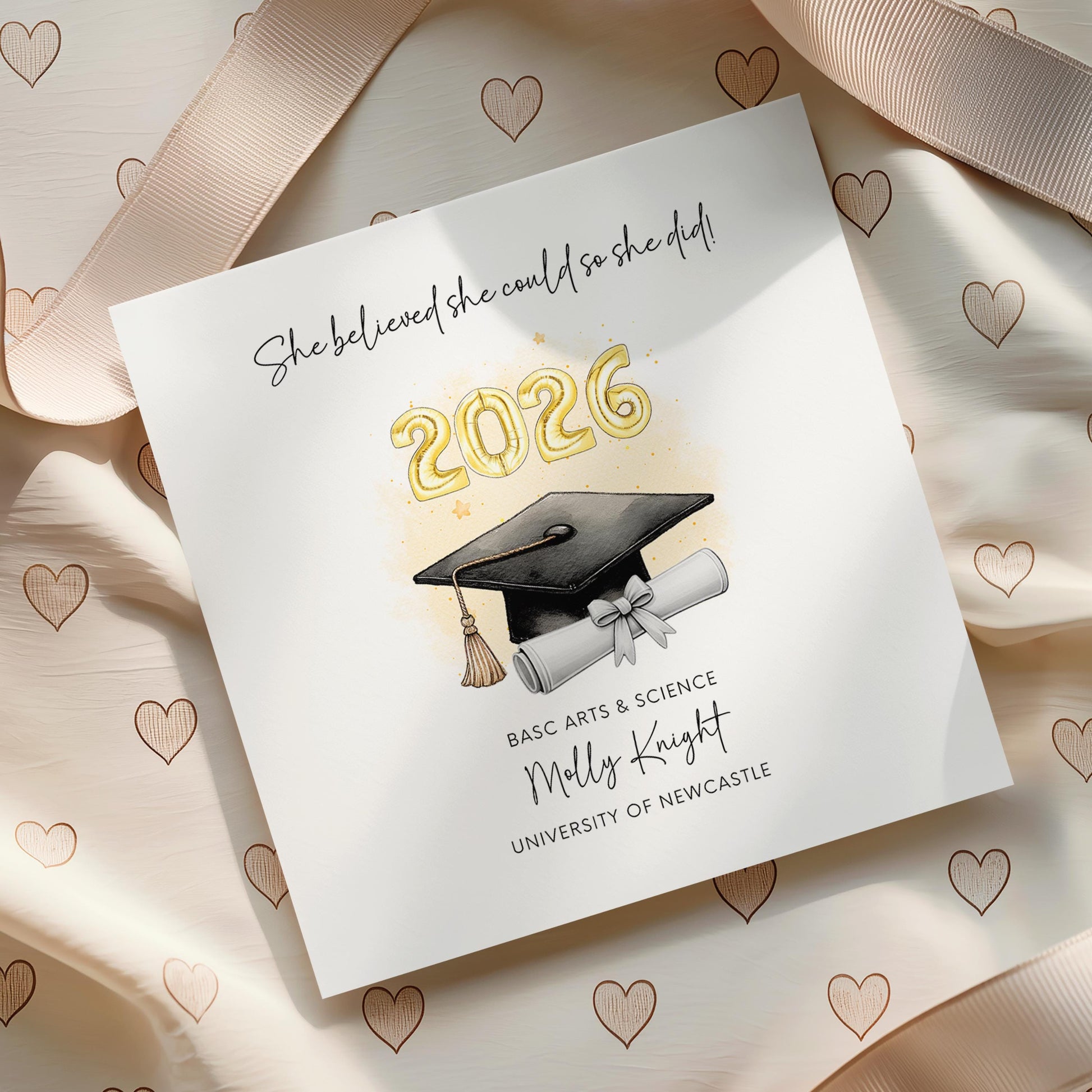 Personalised graduation card for her featuring gold 2026 balloons, graduation cap and diploma scroll. Custom graduate card with degree title, name, university and inspirational graduation quote for Class of 2026.