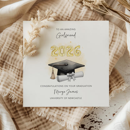Personalised girlfriend graduation card featuring gold 2026 balloons, graduation cap and diploma scroll. Custom university graduation card with girlfriend title, graduate name, university details and congratulations message.