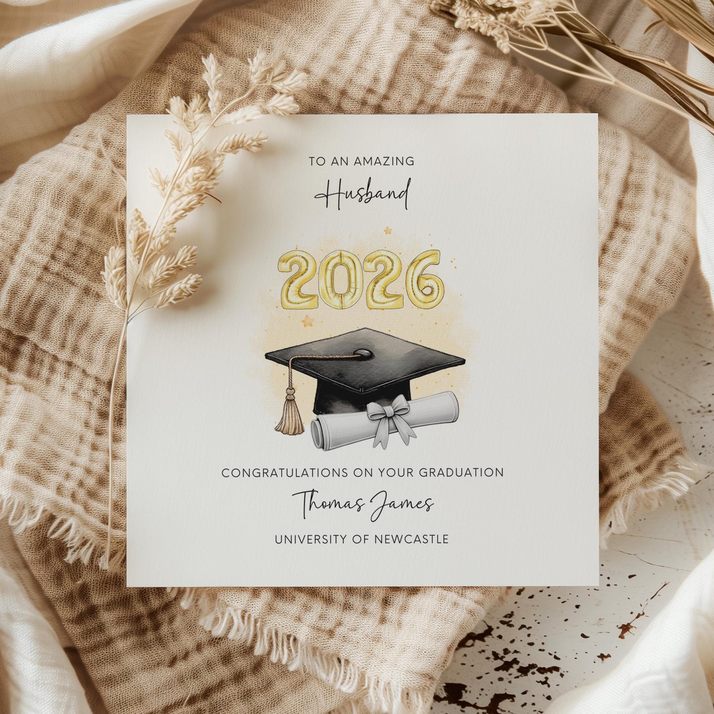 Personalised husband graduation card featuring gold 2026 balloons, graduation cap and diploma scroll. Custom university graduation card with husband title, graduate name, university details and congratulations message.