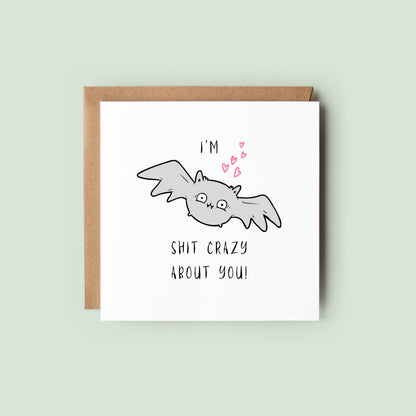 Funny Halloween greeting card featuring a cute grey bat with pink hearts and the humorous message "I'm Bat Shit Crazy About You."