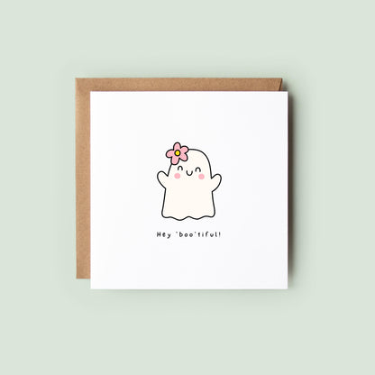Cute Halloween greeting card featuring a smiling ghost with a pink flower in her hair and the playful message "Hey Boo'tiful!"