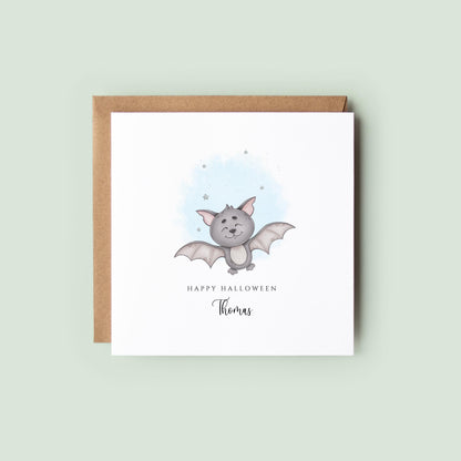 Personalised Halloween card featuring a cute smiling watercolour bat with a custom name underneath and the words "Happy Halloween" on a white greeting card.