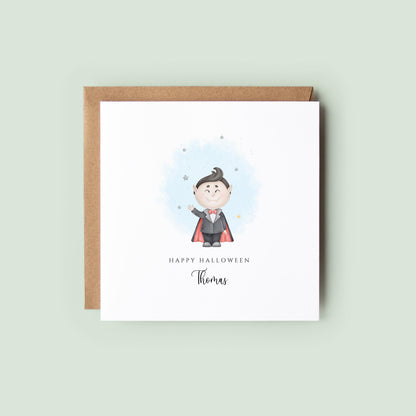 Personalised Halloween card featuring a cute smiling vampire in a cape with a custom name underneath and the words "Happy Halloween" on a white greeting card.